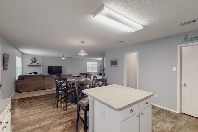 kitchen with pendant lighting, white cabinets, hardwood / wood-style flooring, a center island, and a textured ceiling