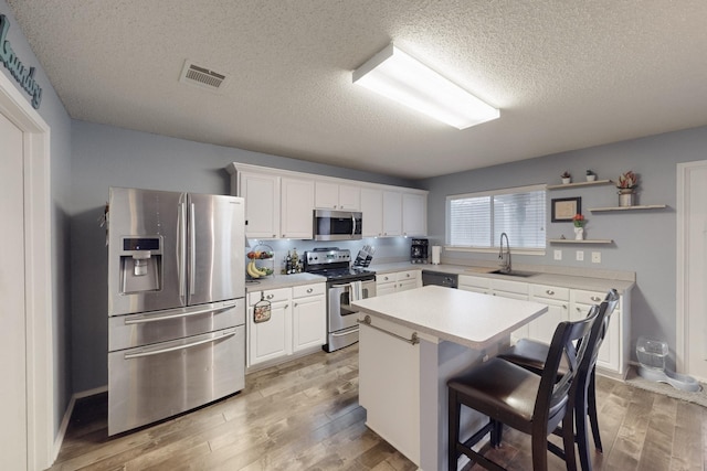 kitchen with appliances with stainless steel finishes, a breakfast bar, sink, white cabinets, and a center island