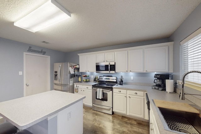 kitchen featuring hardwood / wood-style floors, sink, white cabinets, a center island, and stainless steel appliances