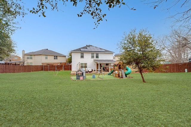 rear view of property with a playground, a lawn, and solar panels