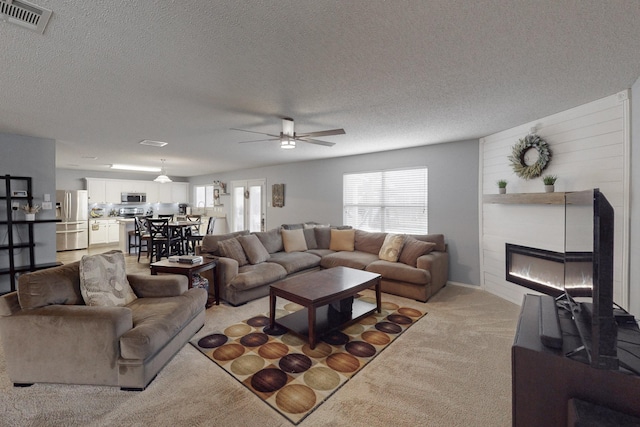 carpeted living room featuring ceiling fan, a large fireplace, and a textured ceiling