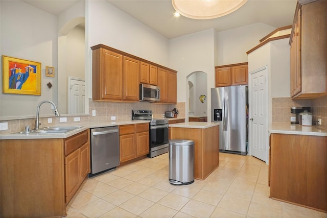 kitchen with light tile patterned flooring, a kitchen island, tasteful backsplash, sink, and stainless steel appliances