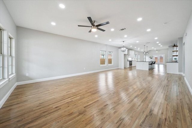 unfurnished living room featuring ceiling fan with notable chandelier and light hardwood / wood-style flooring