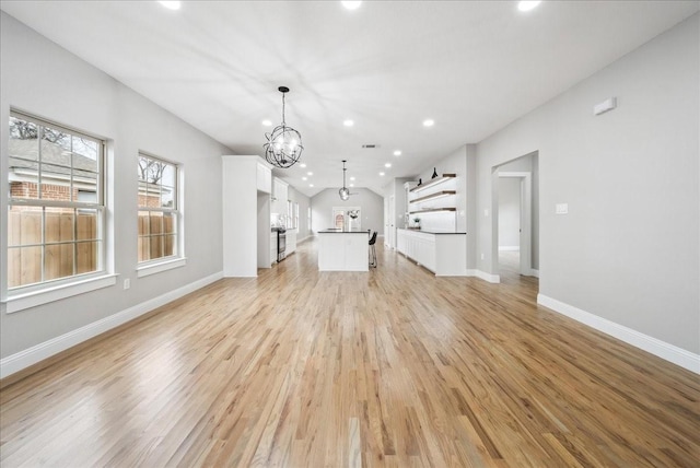 unfurnished living room with a chandelier, vaulted ceiling, and light wood-type flooring