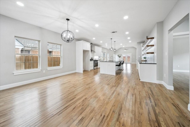 unfurnished living room with a notable chandelier, light hardwood / wood-style flooring, sink, and a healthy amount of sunlight