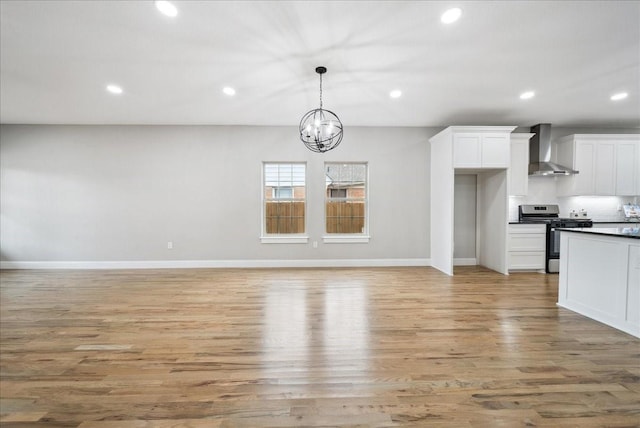 kitchen featuring pendant lighting, stainless steel gas range, white cabinetry, light hardwood / wood-style floors, and wall chimney exhaust hood