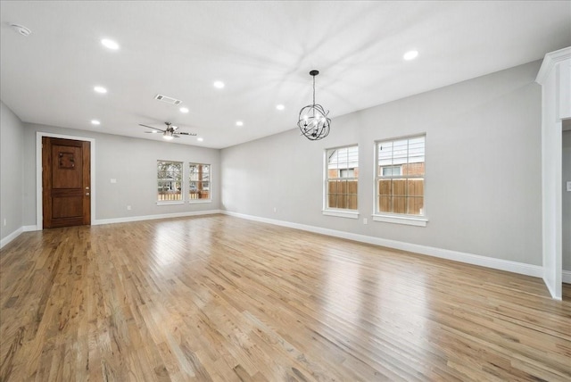 unfurnished living room featuring ceiling fan with notable chandelier and light wood-type flooring