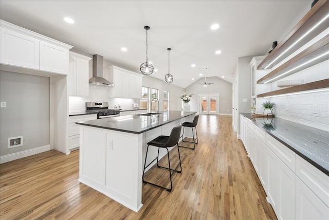 kitchen with wall chimney exhaust hood, sink, stainless steel gas range oven, white cabinetry, and hanging light fixtures