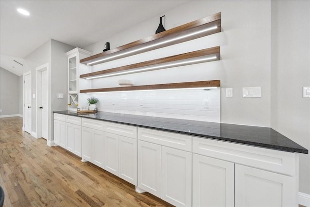 bar featuring white cabinetry, light wood-type flooring, decorative backsplash, and dark stone countertops