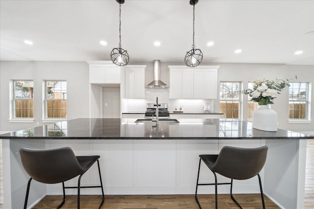 kitchen with white cabinetry, sink, wall chimney range hood, and a large island