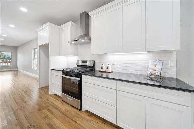 kitchen featuring wall chimney exhaust hood, stainless steel gas range, light wood-type flooring, decorative backsplash, and white cabinets