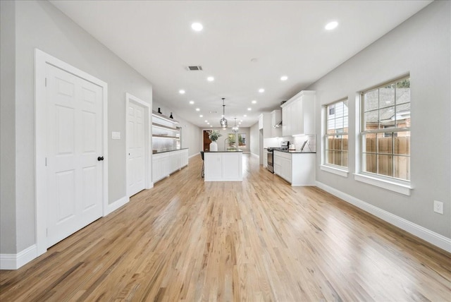 kitchen featuring white cabinetry, hanging light fixtures, light wood-type flooring, stainless steel stove, and a kitchen island