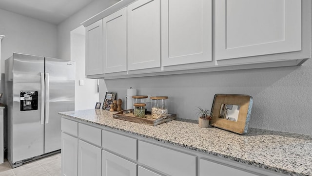 kitchen with light tile patterned floors, stainless steel fridge, light stone countertops, and white cabinets