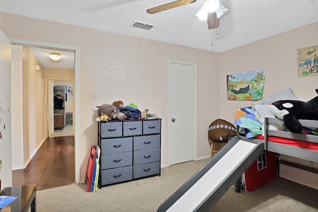 exercise area with ceiling fan, light colored carpet, and a textured ceiling