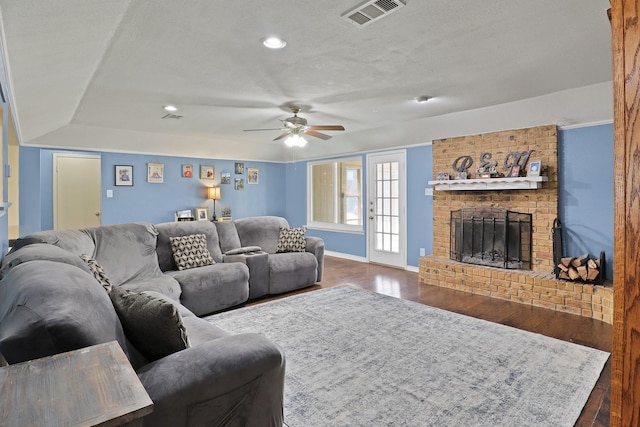 living room with a brick fireplace, dark hardwood / wood-style floors, a textured ceiling, and ceiling fan