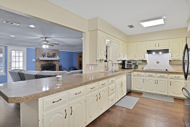 kitchen with dishwasher, sink, kitchen peninsula, gas stovetop, and a brick fireplace