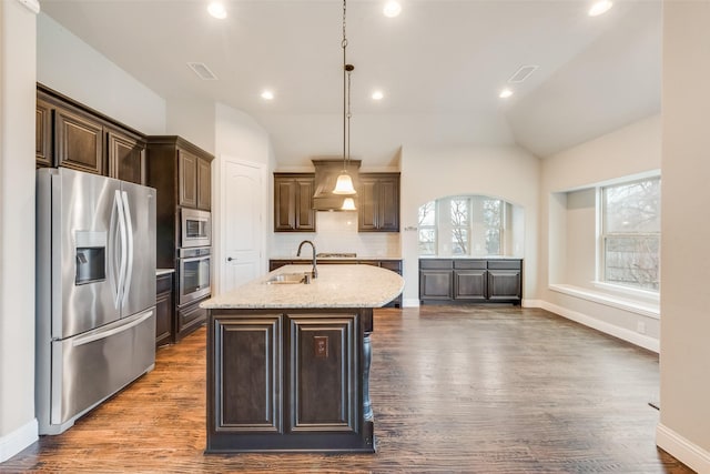 kitchen featuring sink, hanging light fixtures, stainless steel appliances, light stone countertops, and a center island with sink