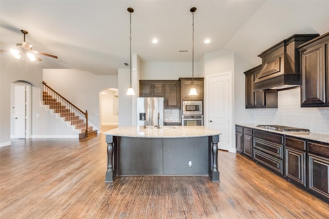 kitchen with appliances with stainless steel finishes, a kitchen island with sink, dark brown cabinetry, and decorative light fixtures