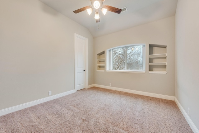 unfurnished room featuring built in shelves, vaulted ceiling, ceiling fan, and carpet