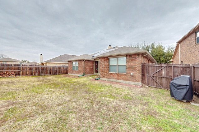 rear view of property with a yard, brick siding, and a fenced backyard