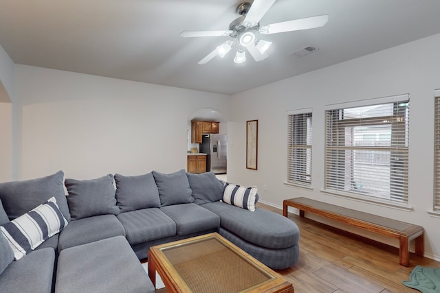 living area featuring arched walkways, light wood-style flooring, visible vents, baseboards, and a ceiling fan