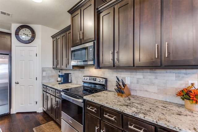 kitchen with dark wood-type flooring, backsplash, dark brown cabinets, stainless steel appliances, and light stone countertops