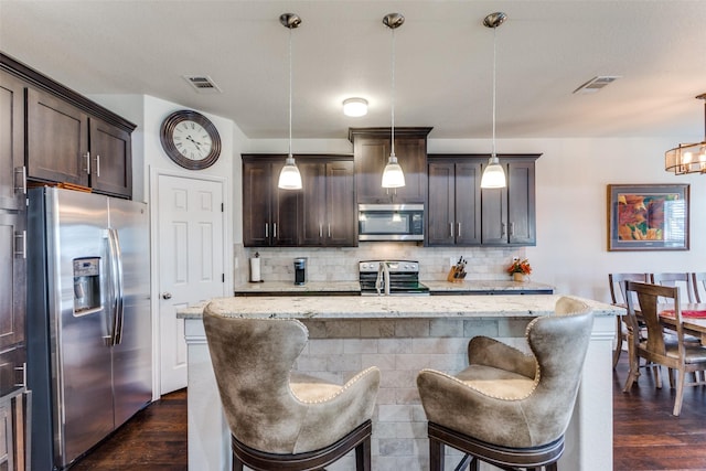 kitchen featuring pendant lighting, a kitchen breakfast bar, stainless steel appliances, and an island with sink