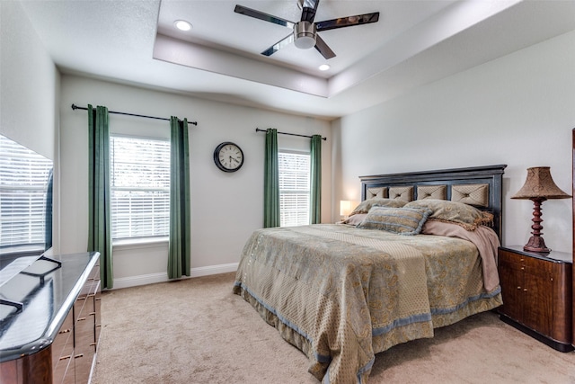 carpeted bedroom featuring multiple windows, ceiling fan, and a tray ceiling