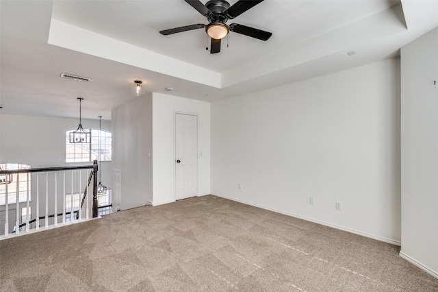 carpeted spare room with a tray ceiling and ceiling fan with notable chandelier