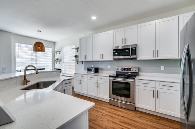 kitchen with sink, white cabinetry, hardwood / wood-style flooring, appliances with stainless steel finishes, and pendant lighting