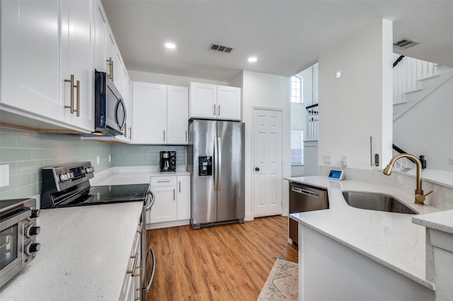 kitchen featuring sink, white cabinetry, stainless steel appliances, light stone counters, and light wood-type flooring