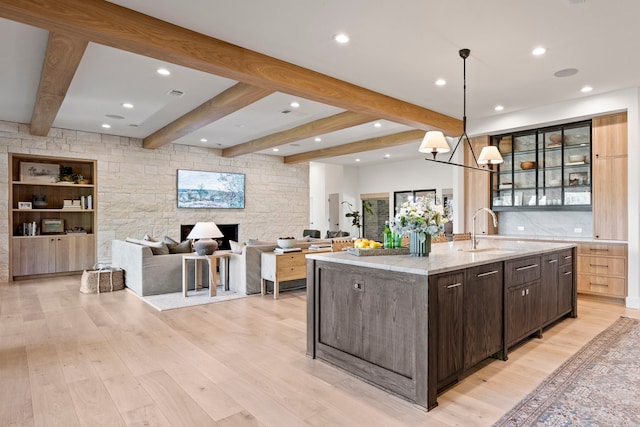 kitchen with a large island, sink, hanging light fixtures, light stone counters, and dark brown cabinetry