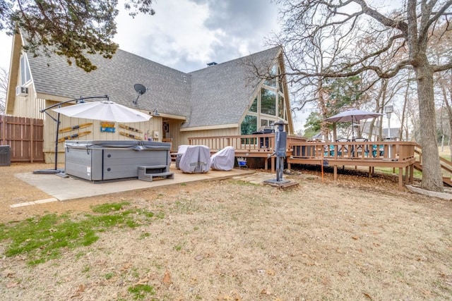 rear view of property featuring a wooden deck, a shingled roof, a hot tub, and fence