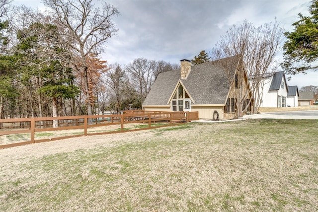view of front of house with a shingled roof, a chimney, fence, a front lawn, and a wooden deck
