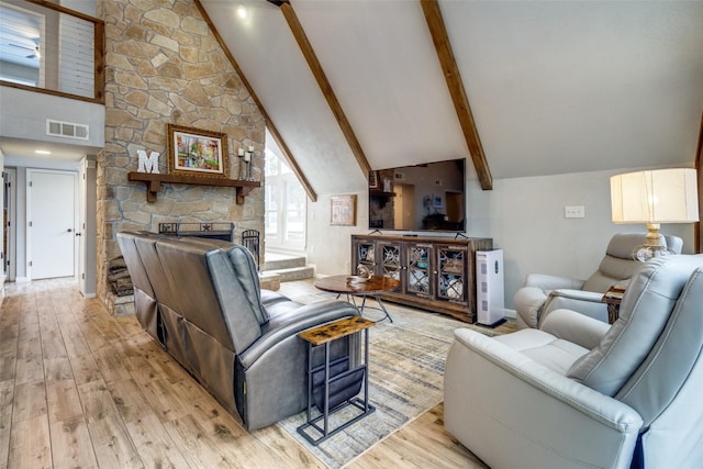 living area with hardwood / wood-style floors, visible vents, high vaulted ceiling, beam ceiling, and a stone fireplace