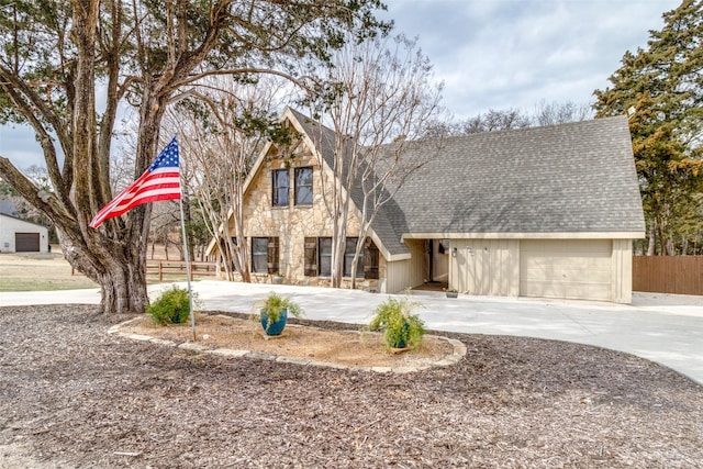view of front of property featuring a garage, roof with shingles, fence, stone siding, and concrete driveway