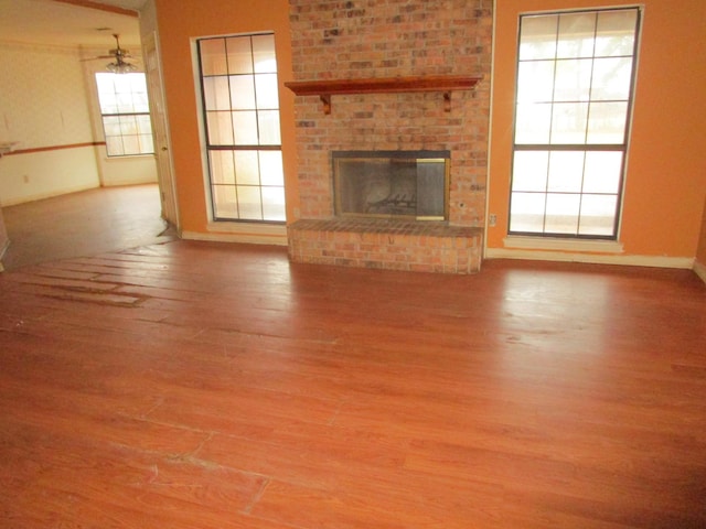 unfurnished living room featuring hardwood / wood-style flooring, a brick fireplace, and a wealth of natural light