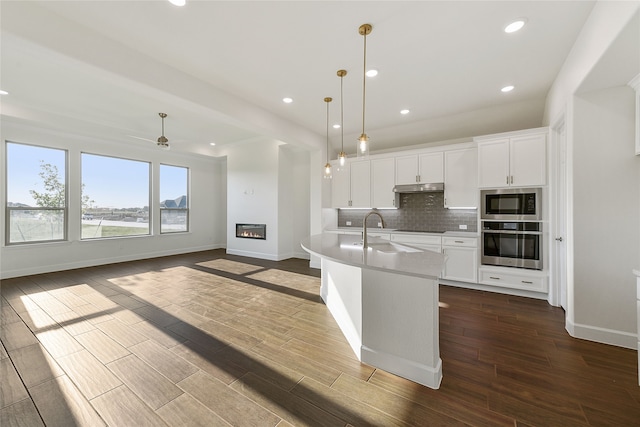 kitchen with built in microwave, stainless steel oven, white cabinetry, and hanging light fixtures