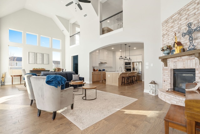 living area featuring baseboards, visible vents, a ceiling fan, a glass covered fireplace, and light wood-style floors