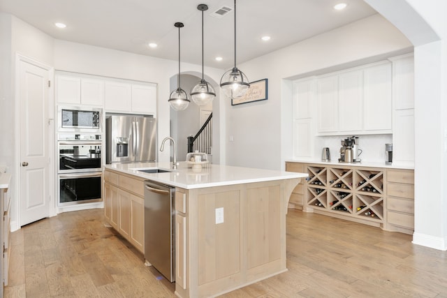 kitchen with white cabinetry, appliances with stainless steel finishes, pendant lighting, and a center island with sink