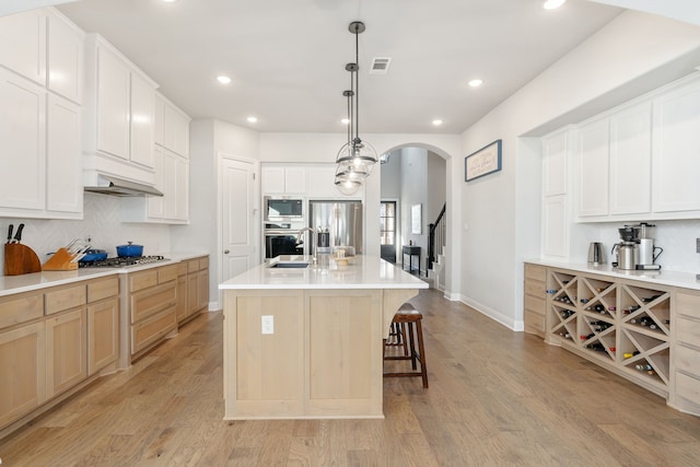 kitchen with pendant lighting, white cabinetry, a kitchen island with sink, stainless steel appliances, and light brown cabinets