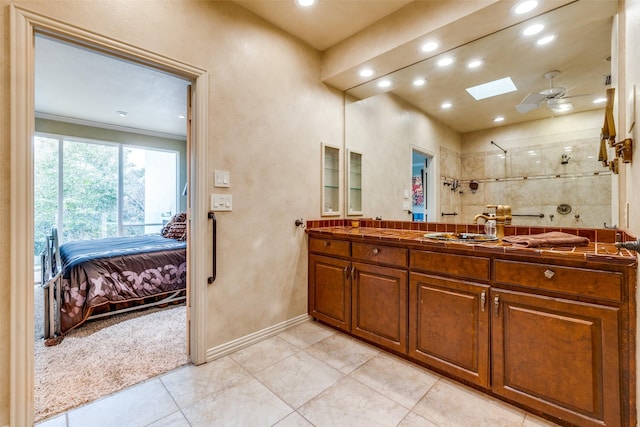 bathroom featuring vanity, a skylight, ceiling fan, and tiled shower