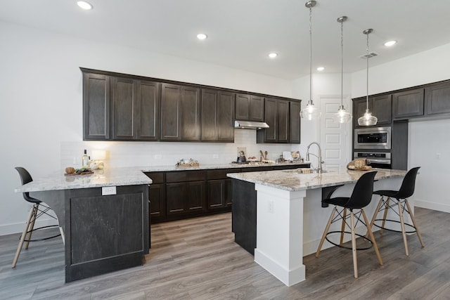 kitchen featuring hanging light fixtures, appliances with stainless steel finishes, a center island with sink, and a kitchen bar