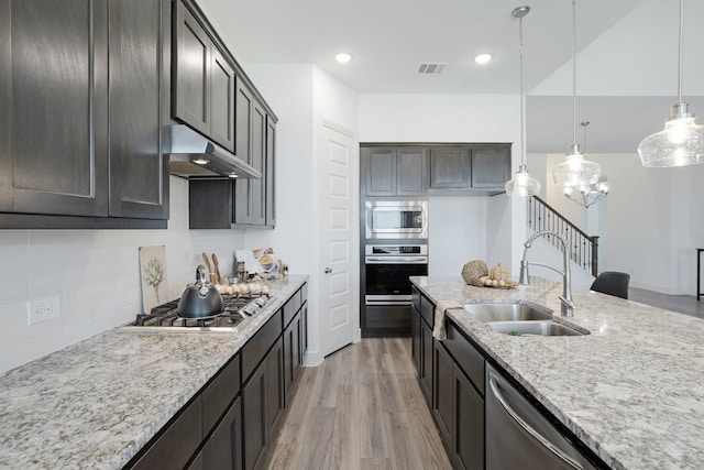 kitchen with pendant lighting, sink, dark brown cabinetry, stainless steel appliances, and light stone countertops