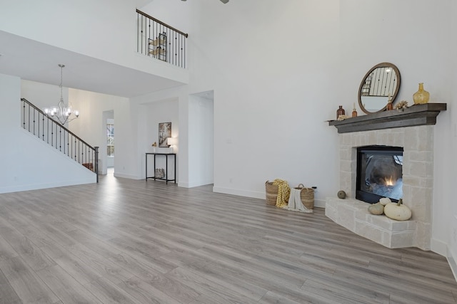 unfurnished living room featuring a fireplace, a high ceiling, light hardwood / wood-style flooring, and a notable chandelier