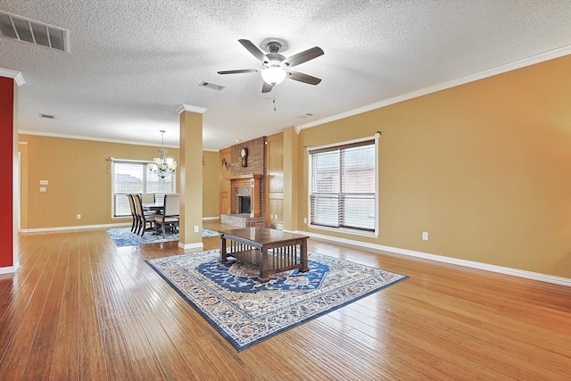 living room with hardwood / wood-style floors, crown molding, ceiling fan with notable chandelier, and a brick fireplace