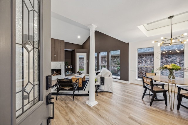 dining space featuring ornate columns, lofted ceiling, a chandelier, and light hardwood / wood-style floors