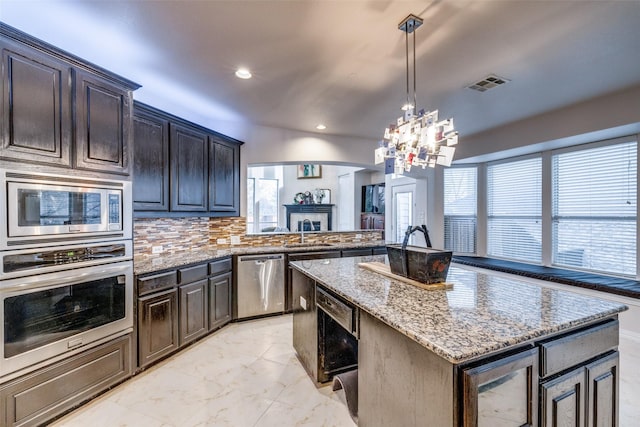 kitchen with pendant lighting, sink, stainless steel appliances, a kitchen island, and decorative backsplash