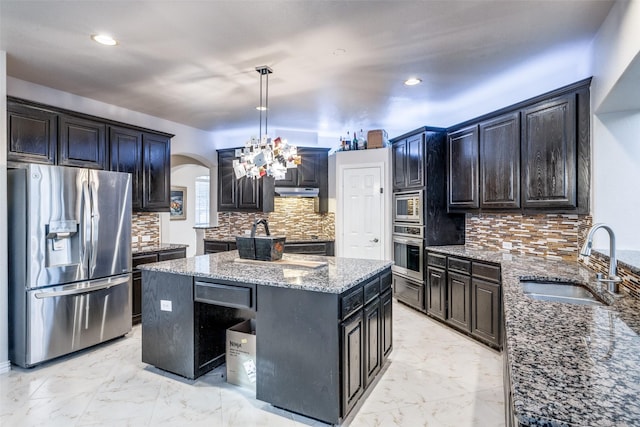 kitchen with stone countertops, pendant lighting, an island with sink, sink, and stainless steel appliances