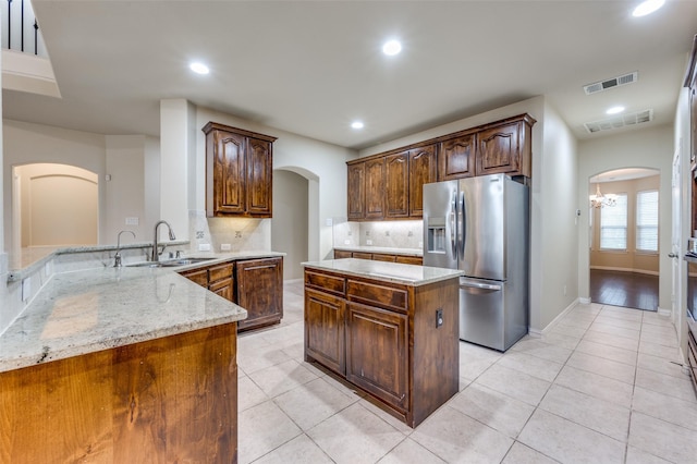 kitchen featuring sink, stainless steel fridge, a center island, light stone countertops, and kitchen peninsula